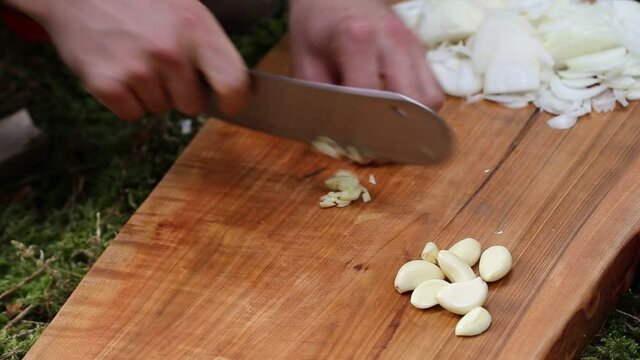 Chopping peeled garlic cloves with a big knife on a wooden chopping board outdoor