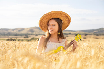 Young woman playing a yellow ukulele in a cereal field at sunset