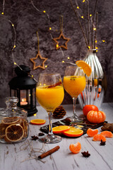 Two glasses of orange juice, cinnamon sticks, black lantern, silver vase, fresh oranges and tangerines on a wooden table