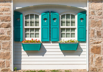 Partial front exterior of white cottage with teal shutters and window boxes with red and white impatiens flowers