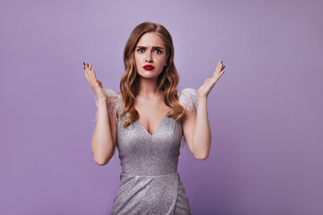 Woman in silver dress looking into camera with misunderstanding. Sad lady in shiny outfit posing on...