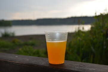 Plastic glass of lemonade on a background of nature, tall grass, a reservoir. Environmental pollution