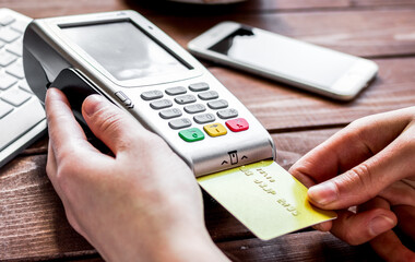 Payment by card in cafe with terminal and keyboard on wooden background