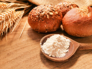 Körnerbrötchen mit Holzlöffel voll Mehl und Getreideähren auf einem rustikalen Holzbrett und Jutesack