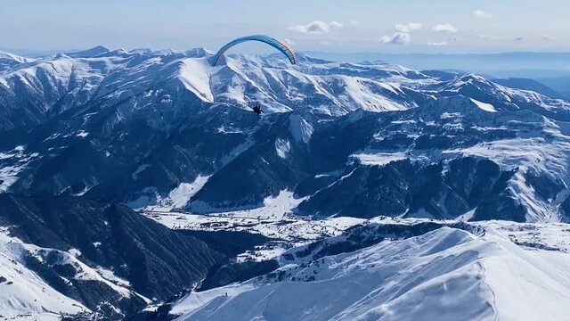 Paroplane fly above winter mountains landscape.