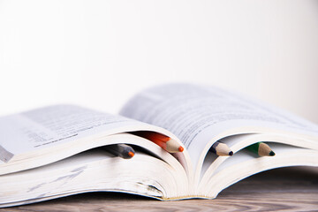 Book with colorful bookmarks with pencils on a wooden table with place for text