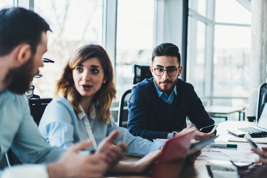 Group of intelligent young people communicating with each other and discussing collaborative process during briefing in office.Male and female employees in formal wear talking about working plan - Powered by Adobe