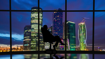 The business woman sits in the office near the windows with a night city view