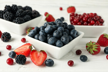 Bowls with berries on white wooden background, close up