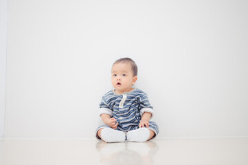 Smiling sitting asian baby boy at home on floor with white background.