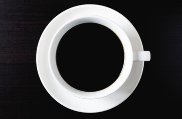 Top view of black coffee in white cup on dark wood flooring