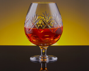 Glass of brandy on a black surface,with yellow gradient background.