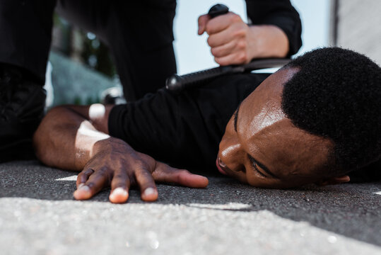 selective focus of detained african american man lying on ground near policeman with baton, racism concept