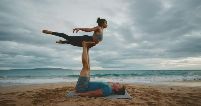 Attractive young couple practicing acro yoga on the beach, healthy wellness fitness lifestyle