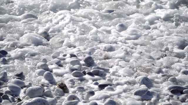 Foamy Ocean Waves Washing Up On The Pebble Beach In Greece.  - close up shot