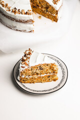Two layered carrot cake slice on a white table and handmade plate. one serving for cake for dessert. garnished with pecans and white frosting  - 364550748