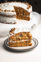 Two layered carrot cake slice on a white table and handmade plate. one serving for cake for dessert. garnished with pecans and white frosting  - 364550799