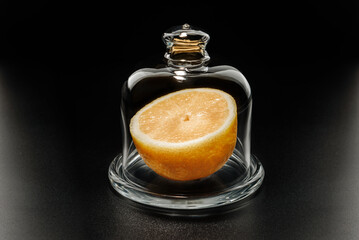 Half a lemon in a glass dish on a black background.