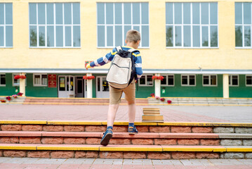 Portrait of a schoolchild with backpack leaping . the boy runs a backpack around the school yard.Childhood, education learning concept