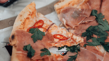Close up shot of slice of italian pizza with copy space. Dish with hot chili pepper, parsley, boiled pork, parmesan, chicken and salami. Delivery restaurant food concept.