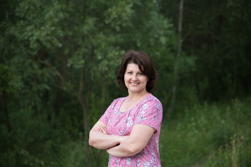 Middle-aged Woman in a pink dress on a summer forest background
