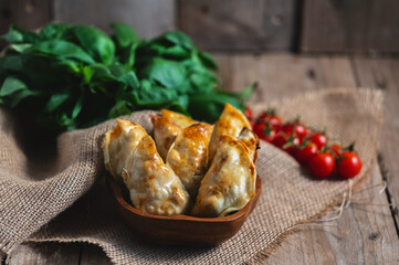 From above of traditional Spanish homemade turnovers served in bowl on rustic wooden table with fresh spinach and tomatoes