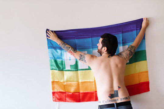 young caucasian boy hanging a rainbow flag of peace in a white room.