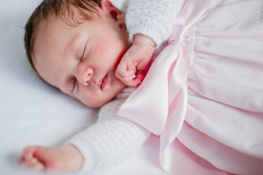 High angle of adorable baby girl in cozy dress lying in cot while sleeping