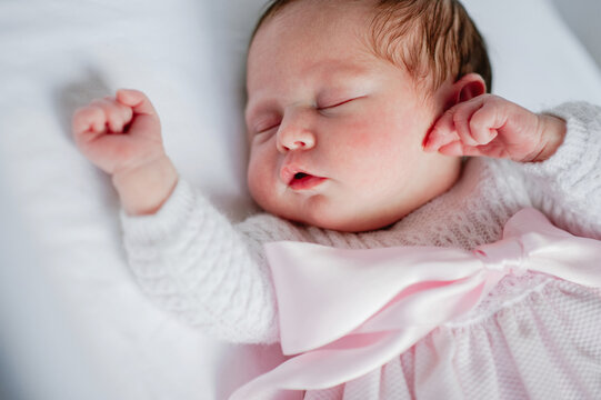 High angle of adorable baby girl in cozy dress lying in cot while sleeping
