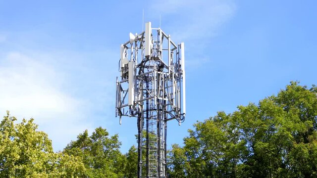 Top of a mobile cell phone mast surrounded by trees against a blue sky. 4k. Hertfordshire. UK