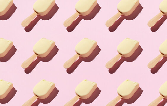 From above of pattern of popsicles placed in rows on pink background in studio