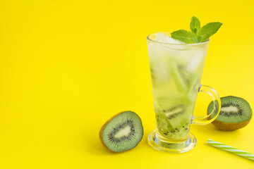 Cold lemonade or infused water with kiwi in the glass  on the yellow background. Copy space.