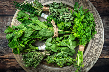 Top view of round plate filled with various fresh green aromatic herbs placed on wooden table