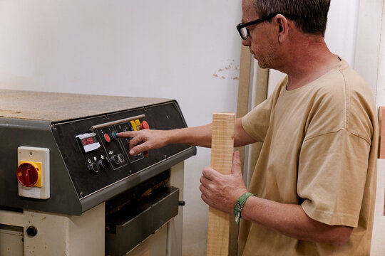 Low angle of woodworker setting up special planning electric machine before using while working with timber in light modern workroom