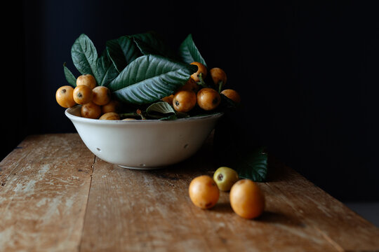 White ceramic plate with tasty natural loquat fruits on branch with fresh green leaves placed on wooden shabby desk