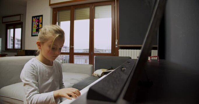Little girl playing piano at home. Kid play piano in living room. Child learning piano at home. Music lesson, medium shot front view.