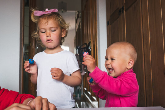 Cute cheerful little kids in casual clothes playing with plasticine while spending time together at home