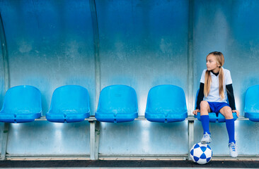 Full length frustrated preteen girl in soccer uniform sitting alone on blue plastic seat after match failure in sports club