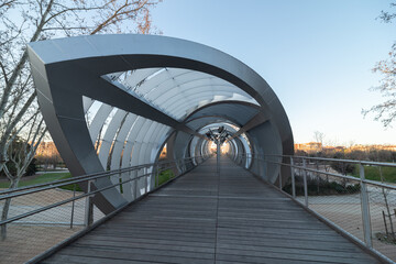 Perspective view of paved wooden bike path going to futuristic gallery in park in city during evening