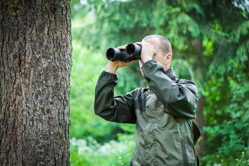 A young hunter in the forest looks into the binoculars. He is trying to find some wild animals.