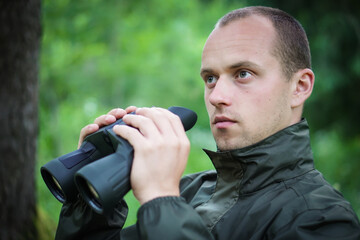 A young hunter in the forest looks into the binoculars. He is trying to find some wild animals.