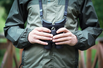 Close up of a man dressed in a hunter jacket holds binoculars in his hand.