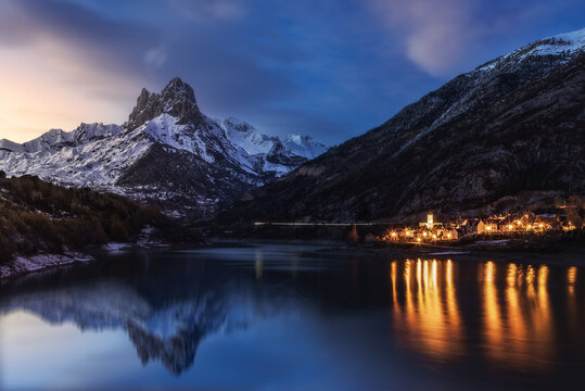 Magnificent view of mount covered partially with snow and reflecting in lake with pure water located near village houses at nightfall