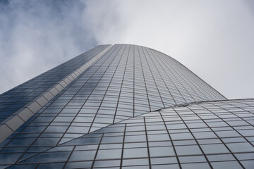 Low angle of contemporary high rise building facade with glass exterior under white cloudy sky in modern city district