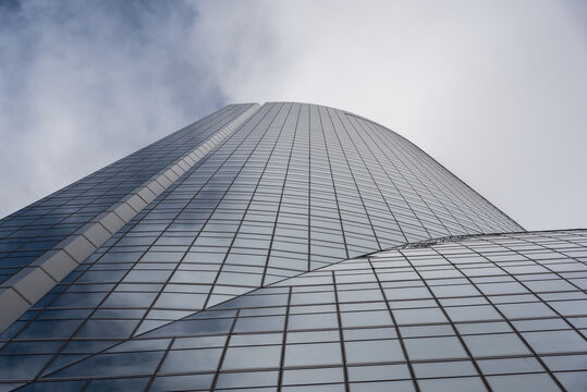 Low angle of contemporary high rise building facade with glass exterior under white cloudy sky in modern city district