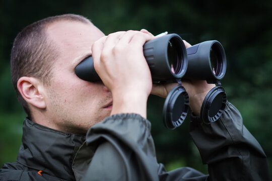 A young hunter in the forest looks into the binoculars. He is trying to find some wild animals.