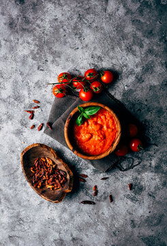 From above of colorful arrabiata sauce decorated with fresh basil near wooden boat shaped plate with sun dried tomatoes and bunch of ripe cherry tomatoes on shabby table