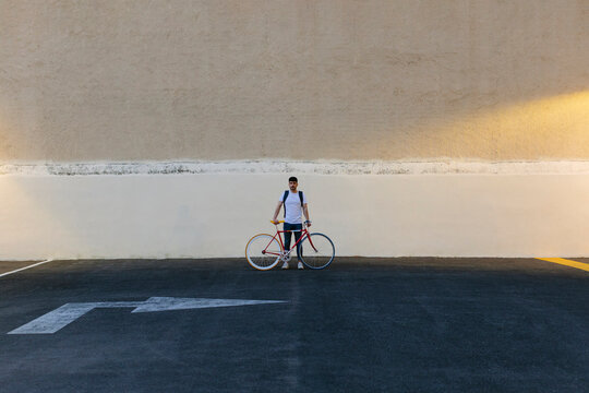 Man with a bike in the middle of a car park at last hour of the day.