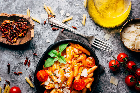 Top view of delicious pasta decorated with ripe cherry tomatoes and fresh basil near wooden bowl with arrabiata sauce and grated Parmesan cheese