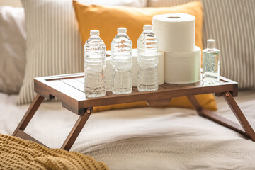Popular household items such as toilet paper, water, and hand sanitizer on a wooden table on top of a bed. Coronavirus pandemic prepping during stay home and shelter in place orders - 364559953